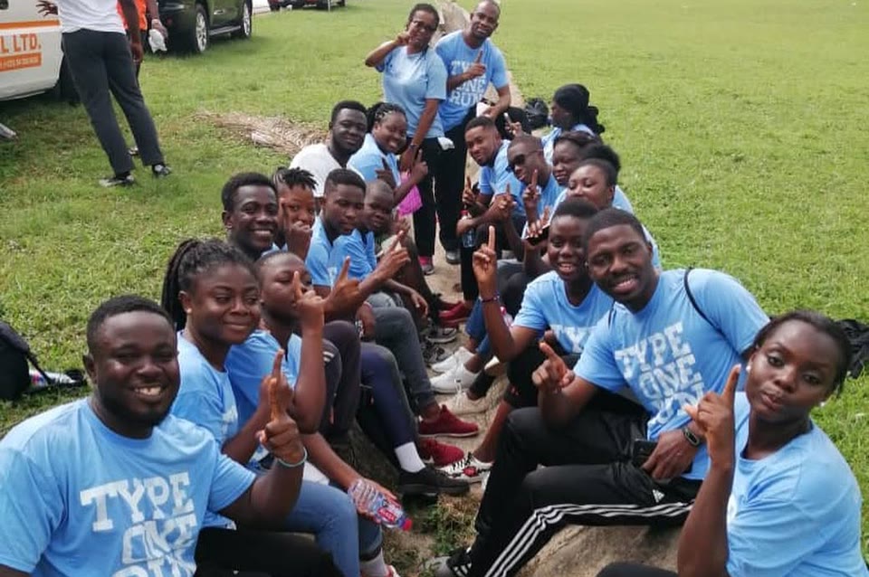 The Accra chapter seated along a grass bank in chapter shirts.